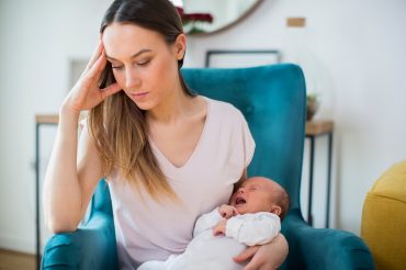 Stressed Mother Holding Crying Baby Suffering From Post Natal De